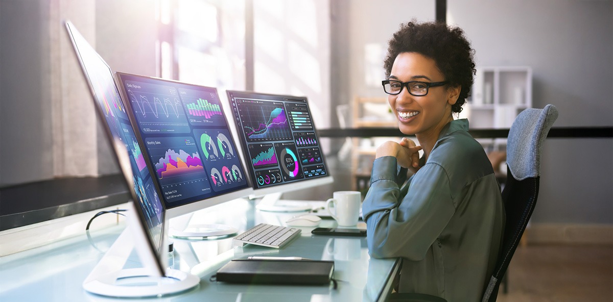 Smiling professional reviewing partner KPIs and performance analytics on dual computer monitors.
