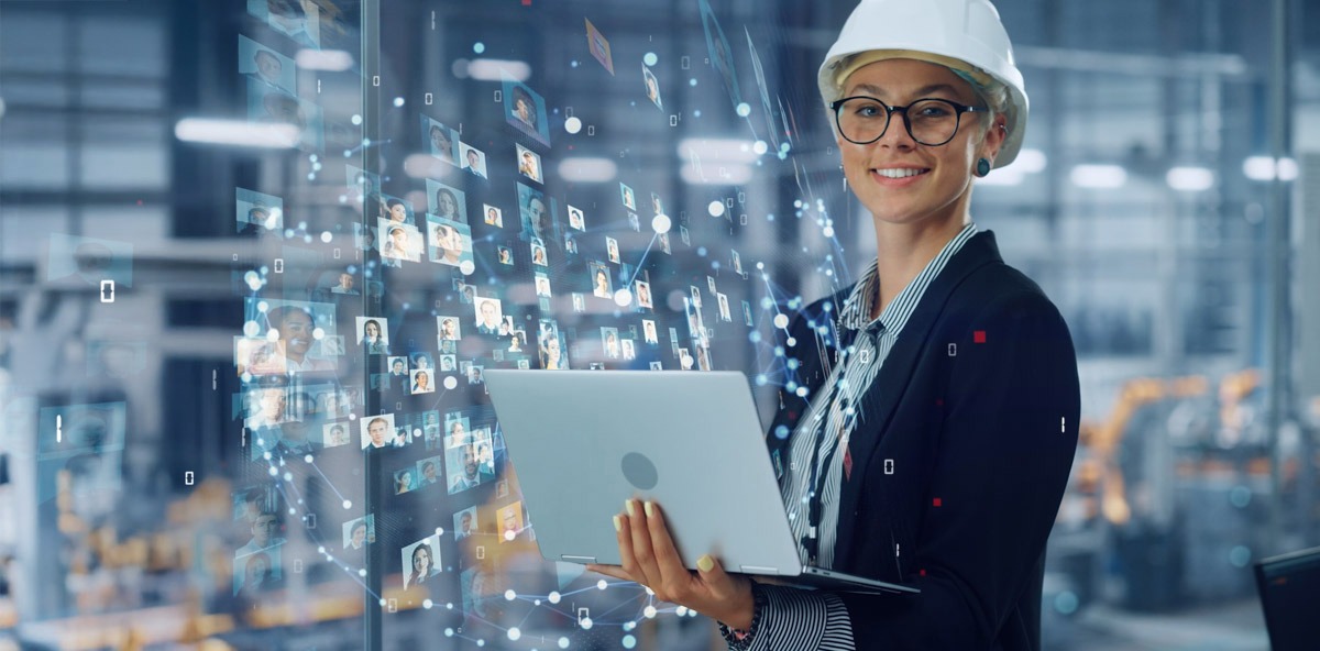 Engineer using a laptop in a smart factory with digital network visuals, representing connected collaboration through Manufacturing Partner Programs.